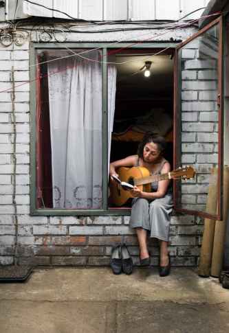 woman sitting on a window and playing the guitar
